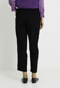 Pantalones negros recortados de ajuste relajado con cintura elástica, combinados con zapatos sin cordones negros con detalles de tachuelas plateadas.