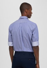 Camicia a righe blu e bianche a maniche corte con risvolti, dotata di colletto con bottoni e vestibilità rilassata. La vista posteriore mostra una finitura liscia.