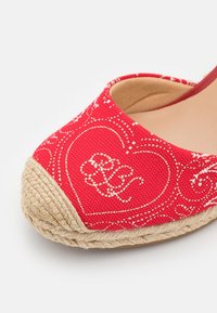 Espadrille en toile rouge avec motif de cœurs et broderie blanche. Détails en corde de jute au niveau des orteils. Doublure intérieure lisse.