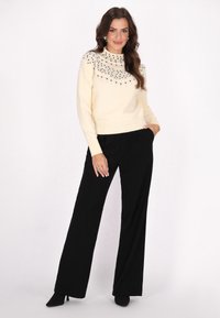 Pulover crem cu embellishments din paiete la decolteu, asortat cu pantaloni negri cu croială largă și cizme negre cu toc.