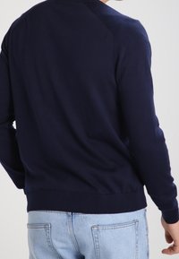 Marinblå stickad tröja med ribbat avslut och ärmslut. Har en slät yta och raglanärmar, designad för en figurnära silhuett.