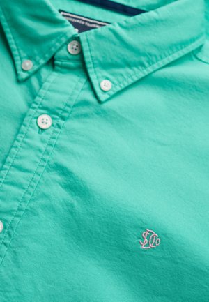 Turquoise button-down shirt made of cotton. Features a standard collar, white buttons, and a small pink logo on the chest. Smooth texture.