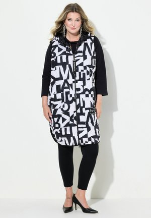 Schwarze und weiße ärmellose gesteppte Weste mit auffälligen Buchstabenmustern, einem Reißverschluss auf der Vorderseite und einer Kapuze, kombiniert mit einem Langarm-Top und schwarzen Leggings.