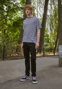 Camiseta gráfica en blanco y negro con el patrón del logo "Levi's", combinada con pantalones negros y zapatillas de deporte en blanco y negro con patrón. Entorno al aire libre.