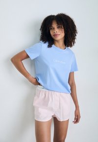 Světle modré bavlněné tričko s bílým logem "Calvin Klein", doplněné světle růžovými šortkami s elastickým pasem. Hladká textura, volný střih.