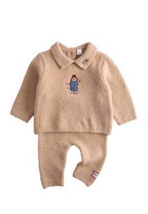 Blødt beige babyoutfit med lange ærmer, krave, broderet bjørn i blå jakke på brystet og rød lap på venstre benmanchet.