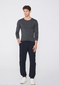 Grauer Langarmshirt und marineblaue Jogginghose aus weichem Stoff. Die Jogginghose hat eine verstellbare Kordelzug-Taillierung und ein Bündchen an den Beinabschlüssen. Weiße Turnschuhe.