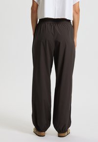 Schwarze, locker sitzende Hose mit elastischem Bund und Bündchen, aus leichtem Material gefertigt. Verfügt über eine glatte Textur.