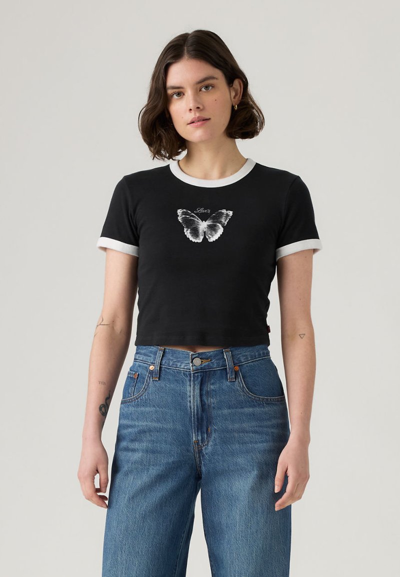 Μαύρο cropped t-shirt με άσπρο γιακά και περίγραμμα στα μανίκια, με γραφικό πεταλούδας στο μπροστινό μέρος. Συνδυασμένο με ψηλόμεσα μπλε τζιν.
