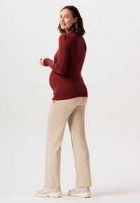 Bluzka ciążowa z ribbed maroon fabric, z długimi rękawami i dopasowanym krojem. Połączona z beżowymi spodniami z szerokimi nogawkami i jasnymi sneakersami.