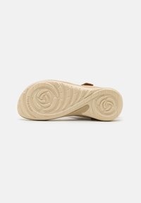 Lys beige skosåle med teksturerte mønstre, som har et spiraldesign. Merket "Merrell" er preget på hælområdet.