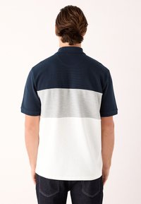 Marineblaues, graues und weißes Poloshirt mit kurzen Ärmeln. Verfügt über Farbblockierung und einen strukturierten Stoff. Kragen mit einer mittigen Rückennaht.