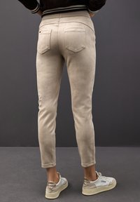 Beige fuskmocka skinnybyxor med bakfickor, smal passform och ribbad midjeband, i kombination med ljusfärgad sneakers.