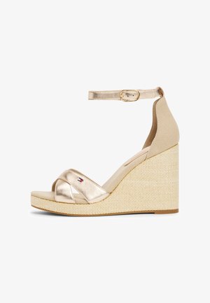 Złote metaliczne sandały na koturnie z paskiem z płótna, z krzyżującym się przodem, klamrą przy kostce oraz teksturowaną naturalną plecioną platformą.