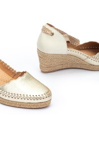 Bottines en cuir doré à talon compensé avec des détails en jute, bout fermé, accents tissés et semelle intérieure texturée. Présente un design à enfiler et une bride élastique à l'arrière.