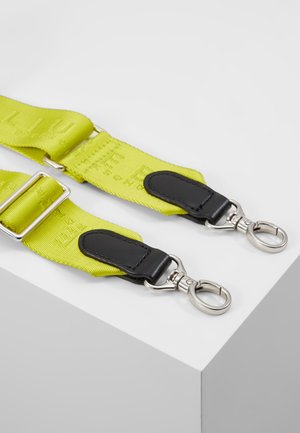 Gul justerbar stofrem med sorte læderdetaljer og sølvfarvede metal drejeled i begge ender på en hvid overflade.