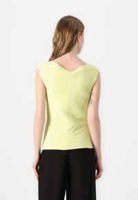 Tett sleeveless topp i lys grønn, med teksturerte horisontale striper, en buet halslinje og en slank silhuett. Kombinert med svarte bukser.