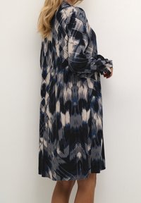 Dlouhé šaty s abstraktním vzorem v námořnické modré, šedé a krémové barvě; lehký materiál; mají volný střih a na zápěstích jsou nařasené.