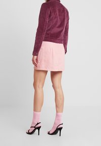 Kordmantel in Dunkelmalve, figurbetontes Design. Rosa Jeansrock mit Taschen-Detail. Rosa Socken und schwarze, riemchenbesetzte High Heels komplettieren das Outfit.