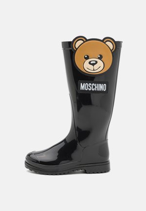 Botte de pluie en caoutchouc noir avec un design de visage d'ours brun à l'avant et une étiquette "Moschino". Semelle texturée pour l'adhérence.