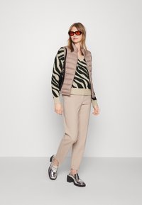 Padded beige liemenė ant zebro rašto megztinio, bežonės kelnės ir sidabriniai mokasinai. Aksesuarai: raudoni akiniai nuo saulės ir juoda rankinė.