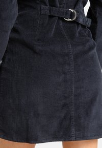 Navy-Baumwollcordkleid mit vertikaler Ripptextur, einem taillierten Gürtel und einem leicht ausgestellten Saum für eine figurbetonte Silhouette.