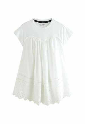 Camiseta blanca de algodón con mangas cortas, que presenta un cuerpo fruncido y un dobladillo de encaje con borde en forma de ondas y patrones florales bordados.