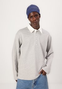 Grå langermet polo-skjorte med hvit krage, med knappelukking og myk tekstur, kombinert med blå jeans og en ribbestrikket lue.