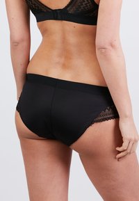 Zwarte onderbroek met een gladde textuur, voorzien van kanten accenten aan de zijkanten en een eenvoudig ontwerp. De tailleband is elastisch voor extra comfort.