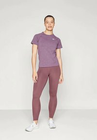 Lilla sport T-särk lühikeste varrukatega ja logoga, koos vormi järgivate, kõrge vöökohaga tumepunaste leggings'itega ja valgete spordijalatsitega.