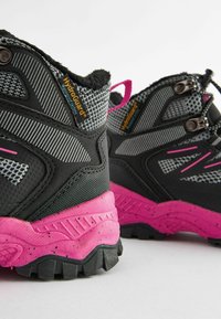 Bottes de randonnée noires et grises avec des accents roses, dotées d'une tige en matériau texturé, d'un talon renforcé et d'une semelle robuste avec des crampons profonds.