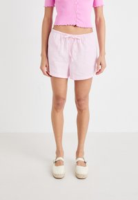 Rozā lina šorti ar elastīgu jostasvietu un auklu. Modelis valkā baltas espadrilles uz gaiša fona.
