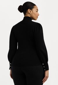 Melnas ribota turtlenecka džemperis ar pūkainām garām piedurknēm un metāla pogu akcentiem pie aprocēm. Redzama teksturēta adīta materiāla struktūra.