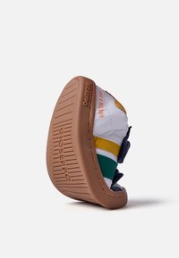 Baskets blanches avec des rayures colorées en jaune, vert et marine, dotées d'une semelle en caoutchouc texturée et d'une sangle velcro réglable.