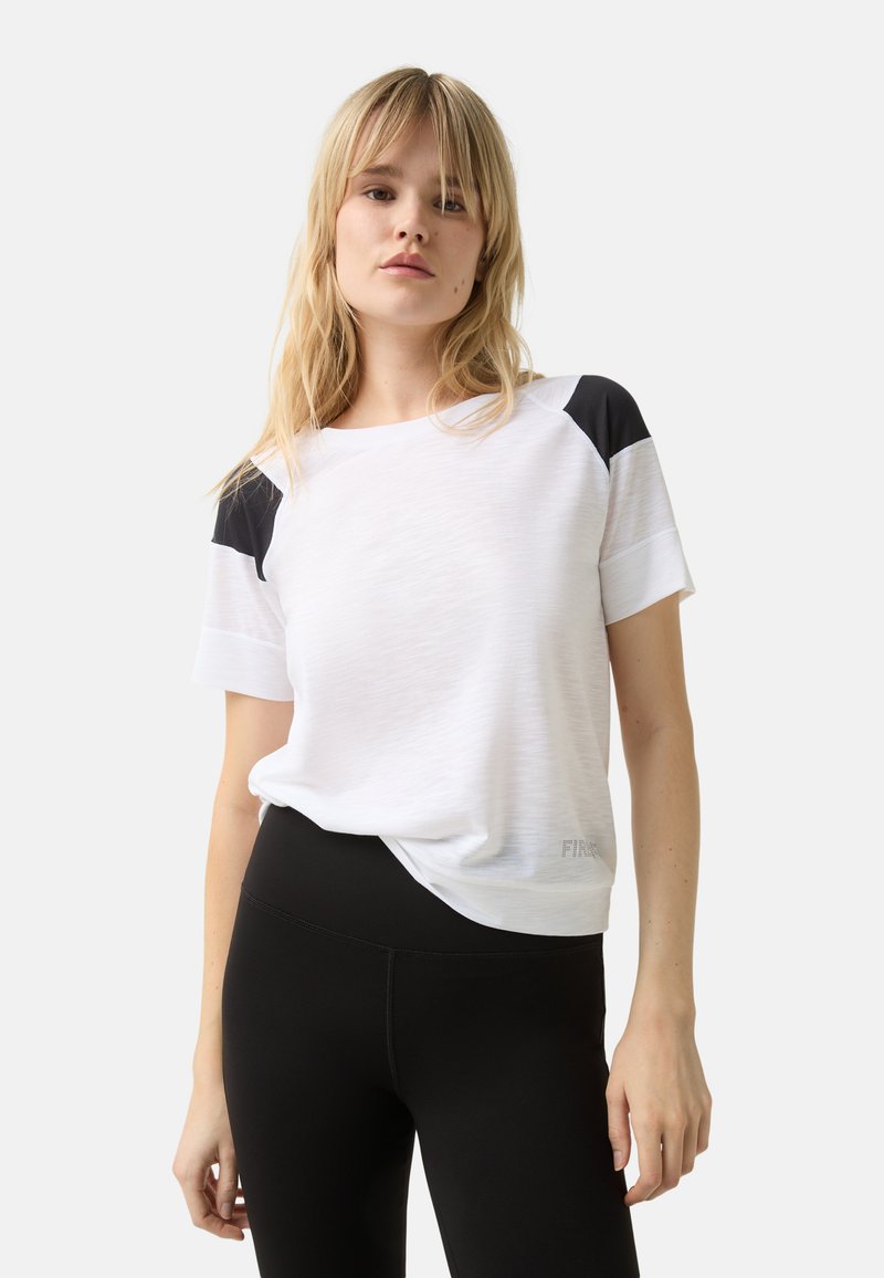 Witte sport t-shirt met zwarte schouderaccenten, korte mouwen en een ontspannen pasvorm. Textuurstof met het woord "FIR" aan de linkerkant onderaan.