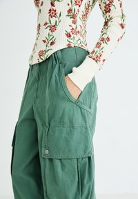 Grønne cargo bukser med løs pasform, der har store sidelommer og et struktureret stof. Kombineret med en langærmet top med rib med blomstertryk.