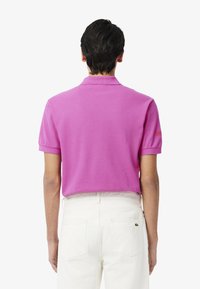 Rosa kort ärmad polo med krage, som har en subtil textur och broderad logotypdetalj på vänster ärm. Bärs med vita jeans.