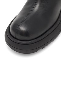 Černá kožená bota s zaoblenou špičkou, zvýrazněným švem a silnou černou gumovou podrážkou. Hladký povrch s minimalistickým designem.