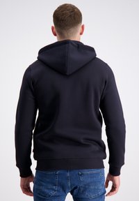 Mænds navy-blue hoodie med en blød tekstur, kengurulomme og ribbede manchetter, båret med blå jeans. Hætten er ujusteret bagpå.