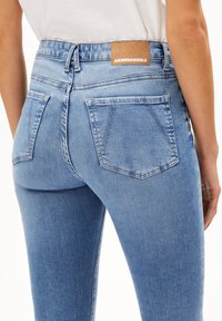 Ljusblå högmidjade jeans i denim, med en läderetikett som har "ARMEDANGELS," två bakfickor och en slät yta.