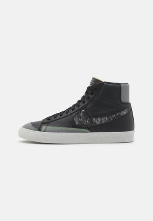 Sort højtop sneaker med tekstureret grå swoosh, grøn syning, sorte snørebånd og hvid sål på en ensartet lys baggrund.
