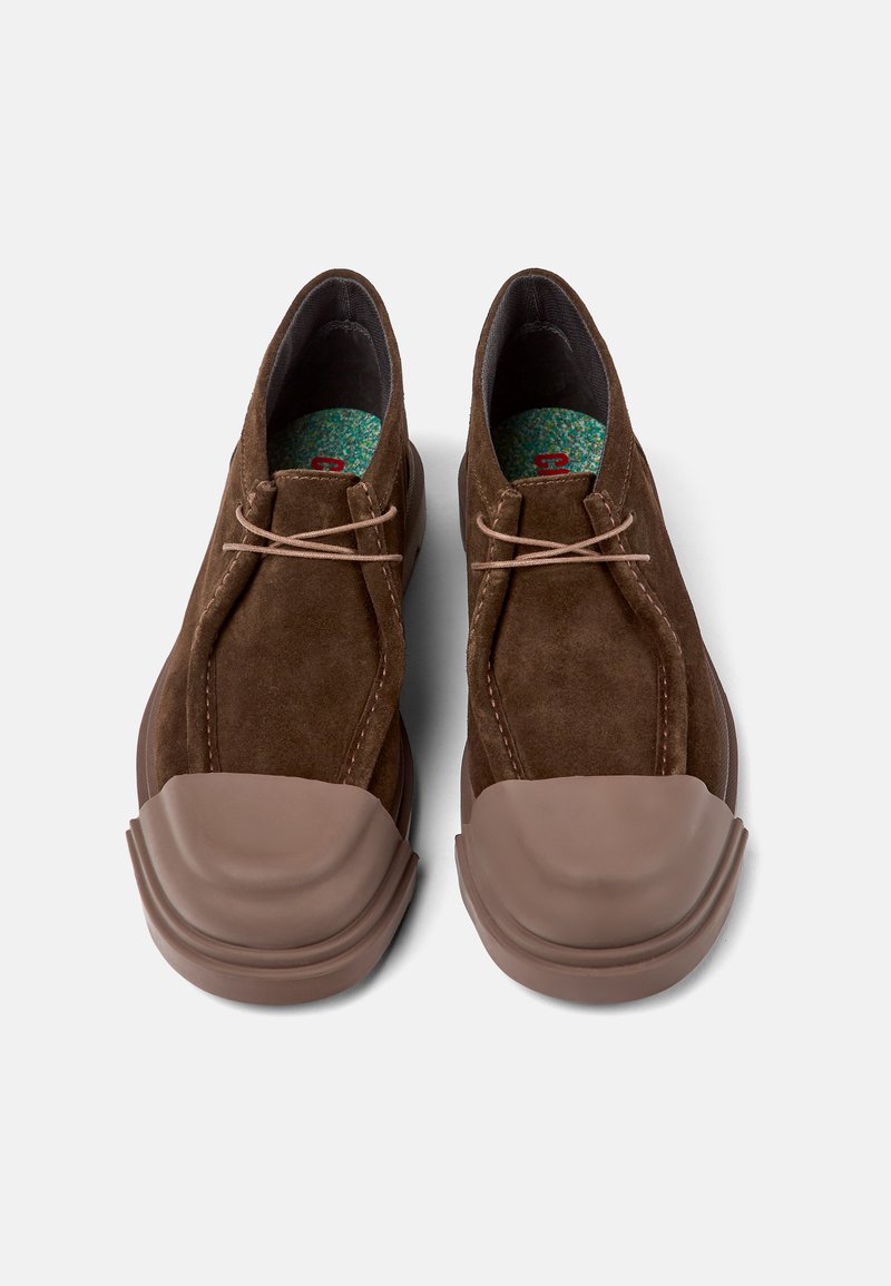 Chaussures en daim marron avec un embout en caoutchouc, présentant une forme arrondie, un design à lacets doubles et une semelle intérieure en teal à motif pour un intérêt visuel supplémentaire.