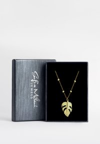 Guldpläterad halskedja med ett bladpendant med utskurna detaljer, hängande från en kedja med runda pärlor, visad i en svart sammetlåda.