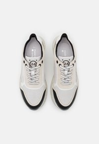 Sneaker bianche e nere con tomaia in mesh perforato, dettagli testurizzati, suola in gomma trasparente e ornamenti neri a contrasto sui lati.