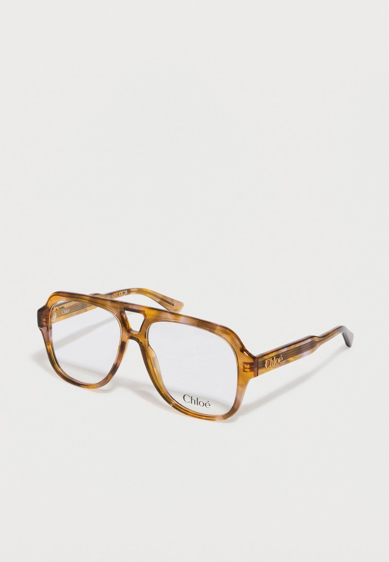 Gafas rectangulares transparentes con montura de acetato marrón claro con diseño carey. Presentan un logo sutil en la varilla y lentes transparentes.