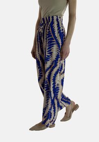 Blå och beige mönstrade vida byxor med elastisk midja, tillverkade av lättviktsmaterial. Bärs med ljusa öppna skor.