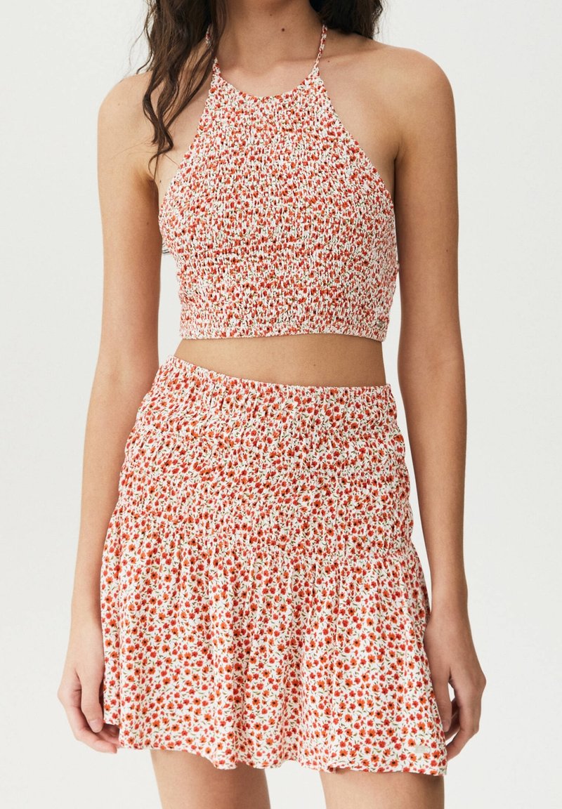 Roter und weißer Blumen-Crop-Top mit Halterneck-Design, kombiniert mit einem passenden Minirock mit elastischem Bund und Rüschensaum.