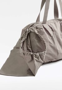 Harmaa, pehmeä kangasduffelilaukku, jossa on kerätty suuaukko, vetoketjukiinnitys ja kaksi kantokahvaa. Tyylikäs, minimalistinen muotoilu.