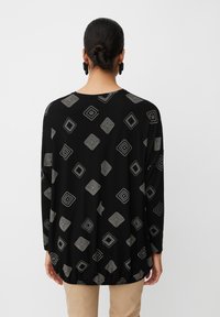 Schwarzes Langarmoberteil mit geometrischen Silbermustern. Weicher Stoff mit rundem Ausschnitt und gerafftem Saum für eine lässige Passform.