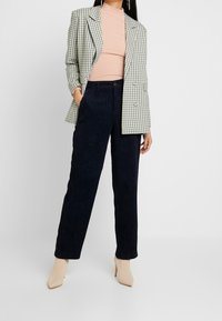 Rutig blazer med ljusgröna och marinblå mönster över en rosa ribbad topp. Marinblå kordflorsbyxor med rak passform och beige högklackade skor.